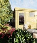 Image (3)AF25x25x211P0PD1F Abri jardin en bois clair avec fenêtre et porte, entouré de verdure luxuriante et d'une piscine
