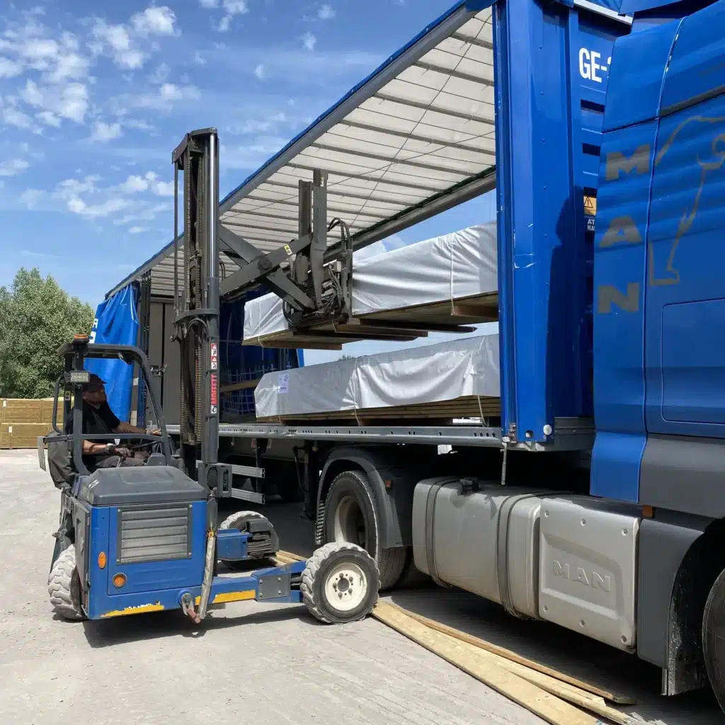 Chariot embarqué déchargeant des panneaux bois emballés d'un camion bleu MAN sous ciel dégagé