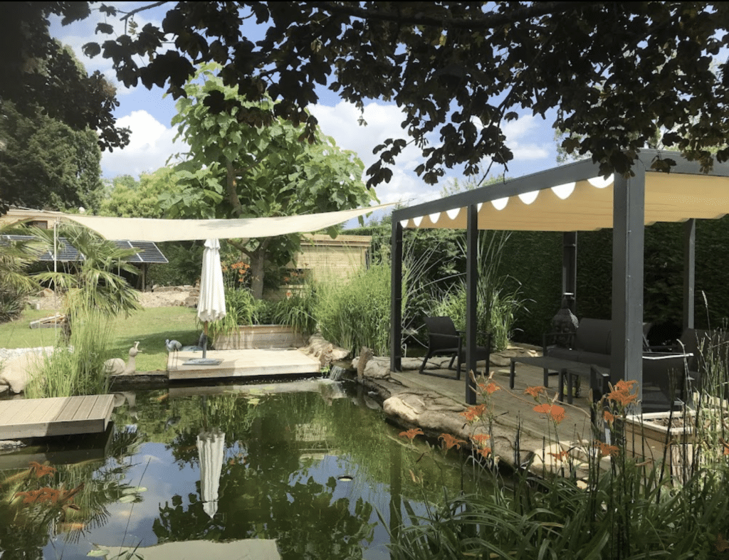 Jardin paysager avec bassin, terrasse abritée et plantation luxuriante sous voile d'ombrage