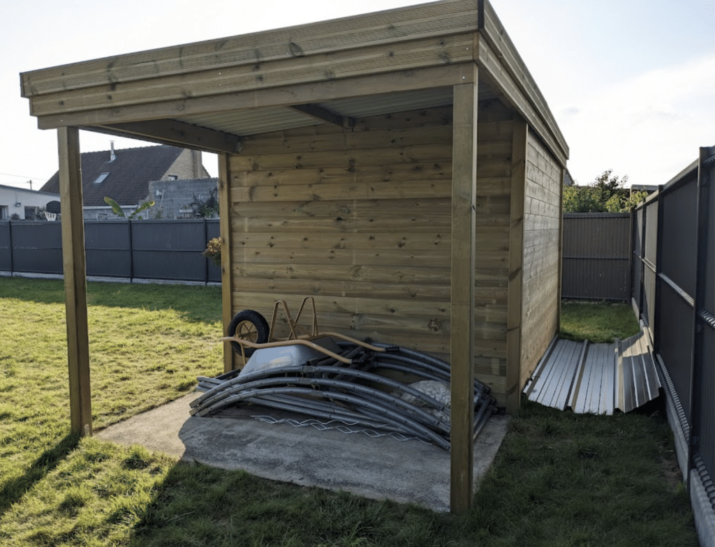 Abri jardin bois avec extension de toit, installation client dans un jardin verdoyant avec brouette et éléments de structure