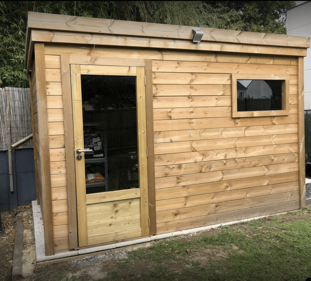Abri de jardin en bois massif avec porte vitrée et fenêtre, installé dans un jardin verdoyant