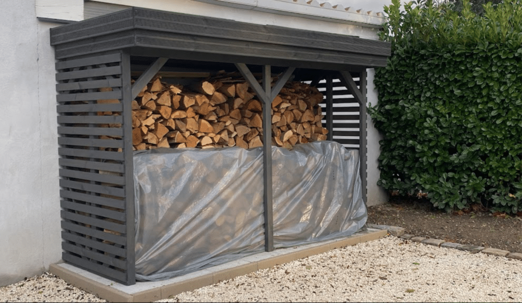 Abri bois de jardin moderne gris foncé, idéal pour stocker du bois, installé dans un jardin paysager