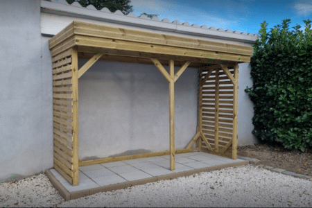 Appentis bois pin sylvestre Abri Français installé sur terrasse carrelée en jardin avec haie verte