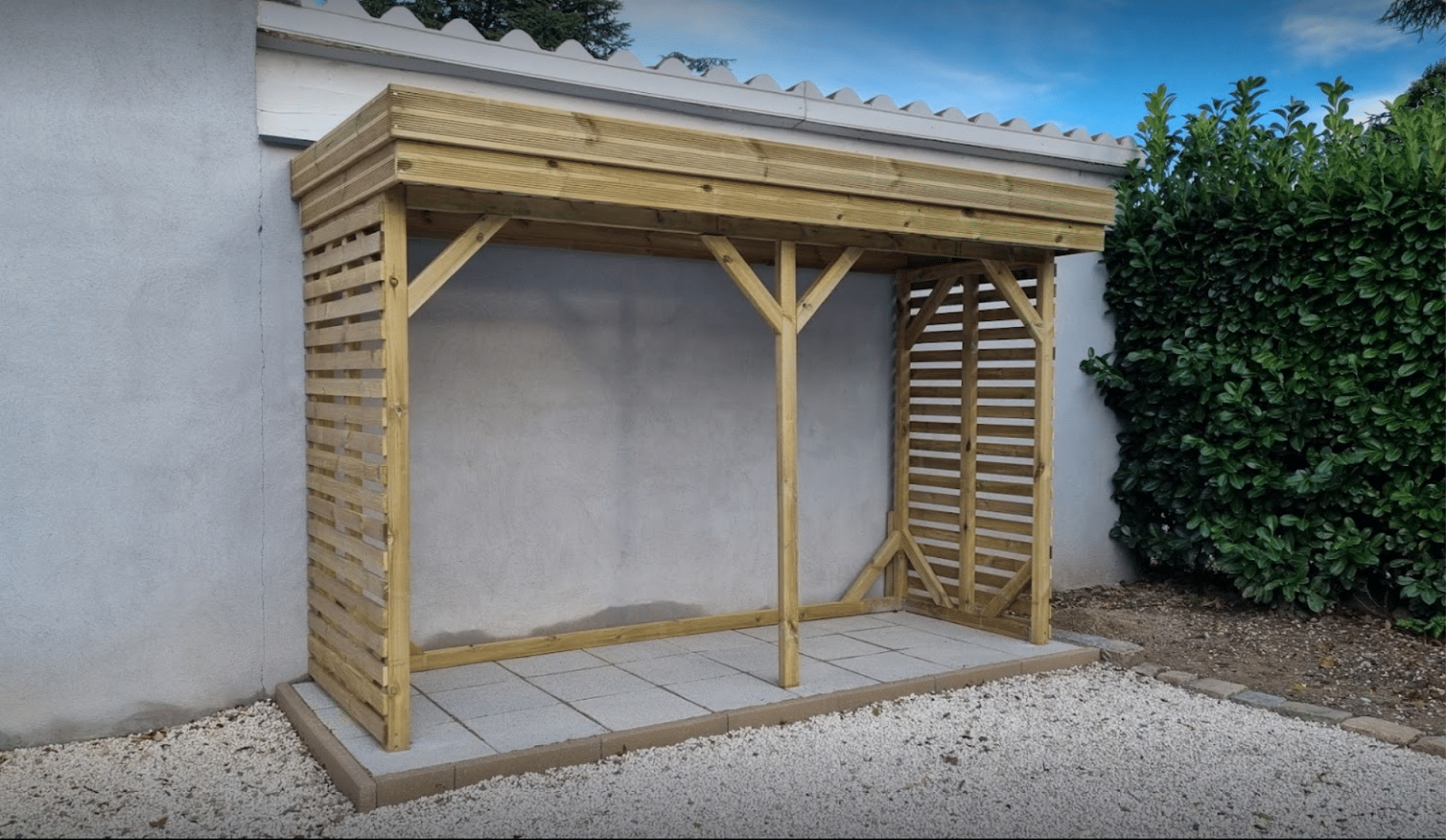 Appentis bois pin sylvestre Abri Français installé sur terrasse carrelée en jardin avec haie verte