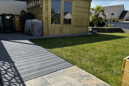 Abri jardin bois double porte vitrée installé dans un jardin avec terrasse, bel aménagement paysager