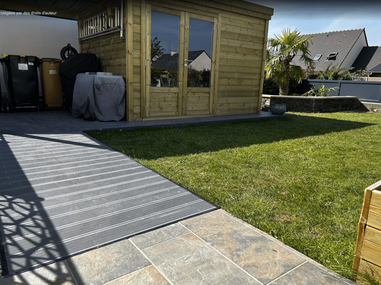 Abri jardin bois double porte vitrée installé dans un jardin avec terrasse, bel aménagement paysager