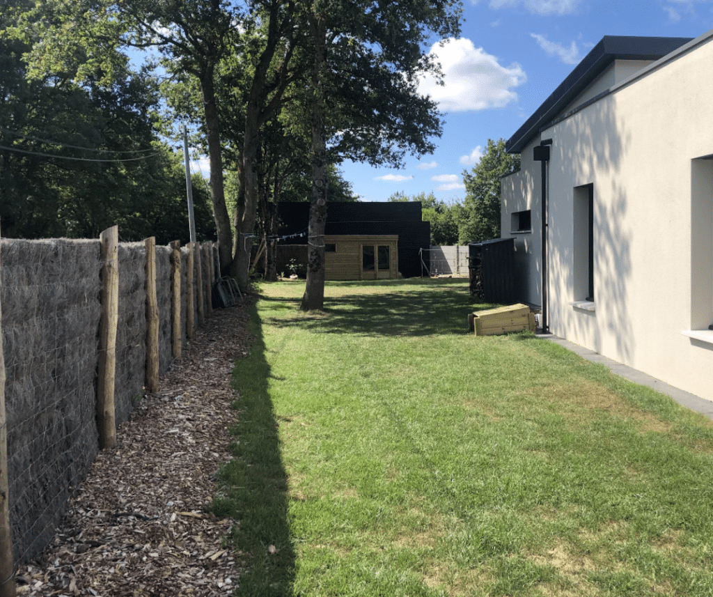 Abri de jardin en bois naturel dans une cour verdoyante avec clôture